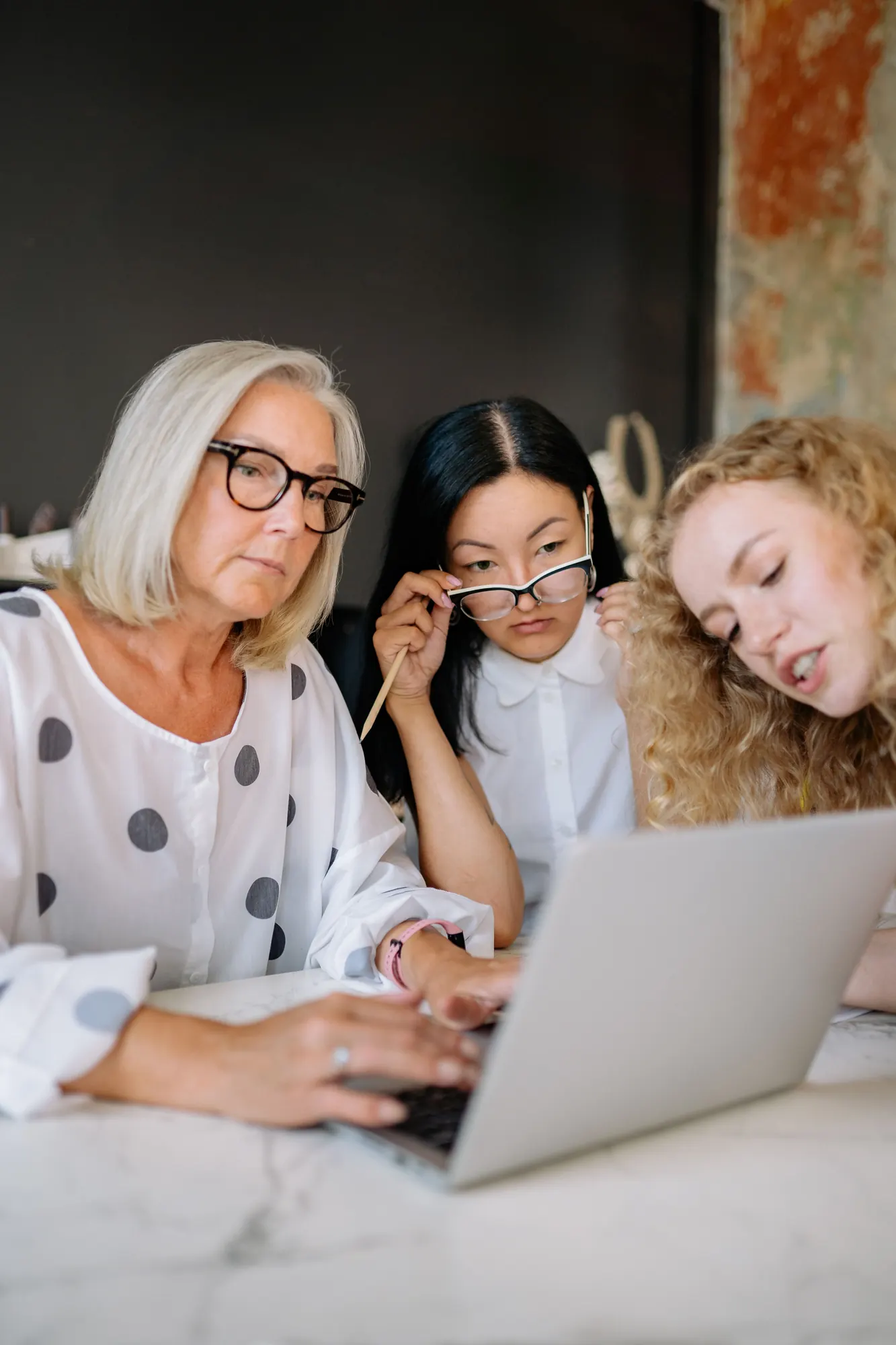 Three women working together around a laptop